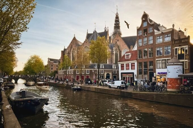 A serene Amsterdam canal lined with historic buildings and a church, framed by trees under a clear sky.