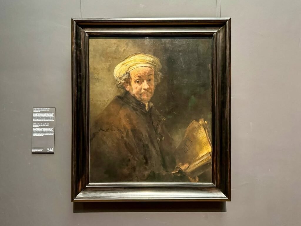 A framed portrait painting displayed on a gray museum wall with an informational placard.