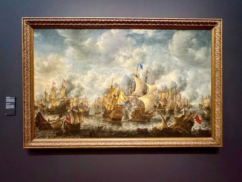 A detailed oil painting of a naval battle in an ornate gold frame, displayed on a gallery wall.