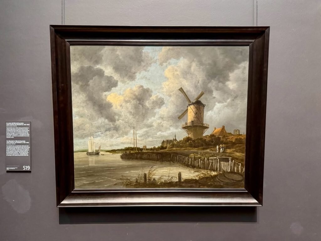 A classic landscape painting of a Dutch windmill by a river, displayed in a dark wood frame.