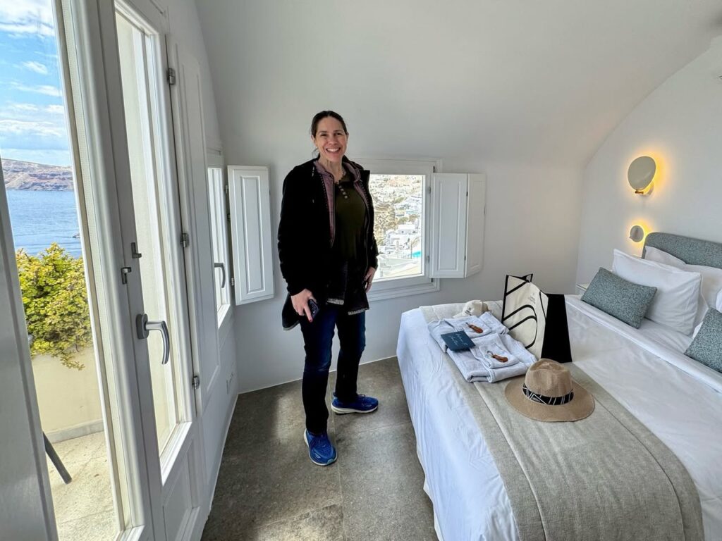 A person stands in a modern bedroom with a large bed, minimal decor, and open windows framing ocean views.