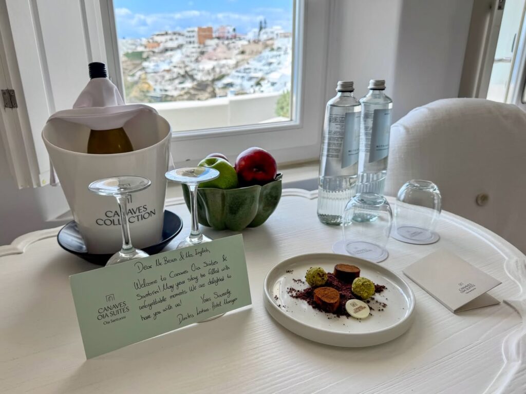 A close-up of hotel room amenities including a wine bottle and fruit bowl on a table by the window.
