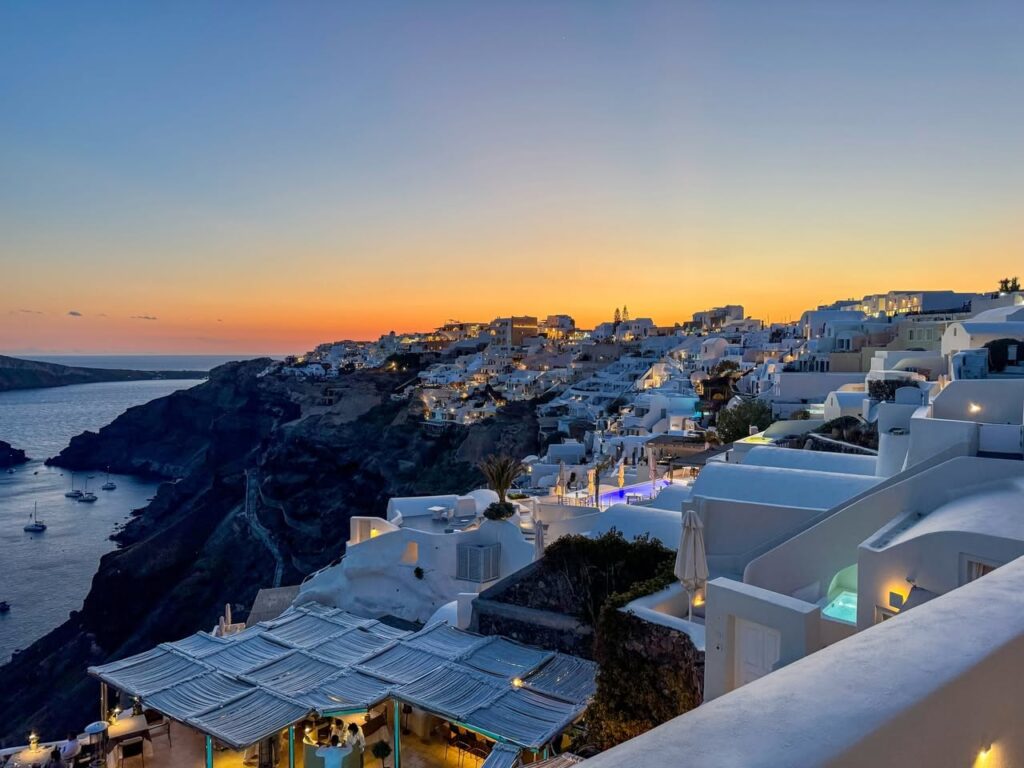 A stunning sunset over the white-washed buildings of Santorini, Greece. The Caldera and ocean waters are visible on the left.