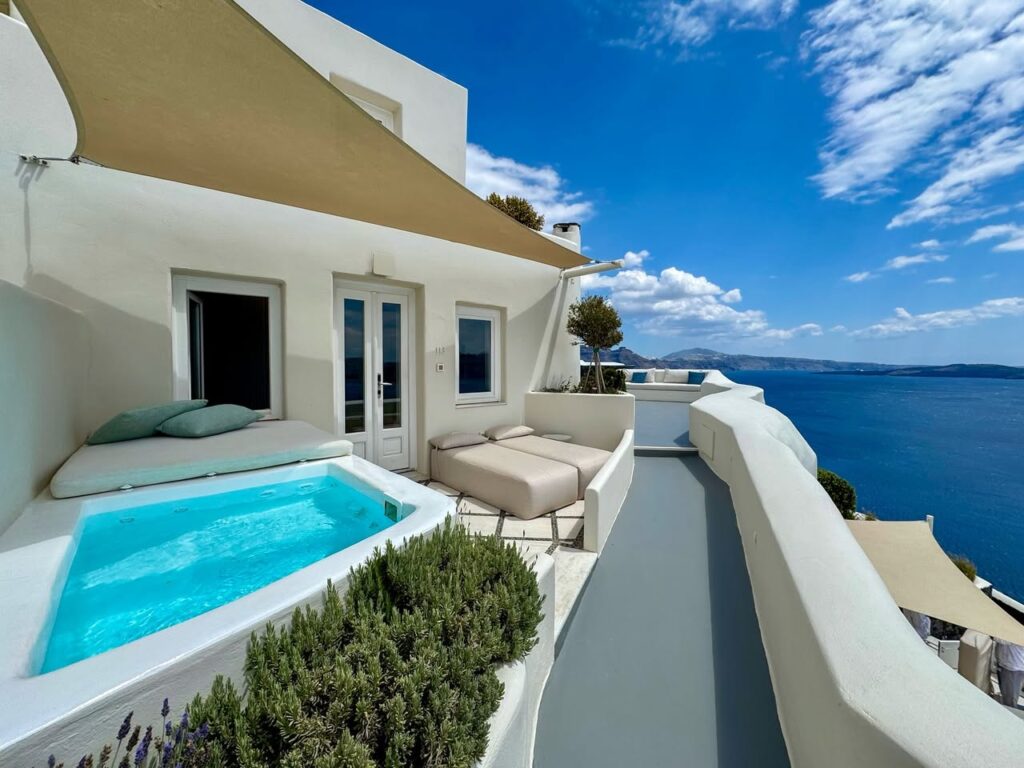 White-washed terrace featuring a private plunge pool and outdoor sofa overlooking the deep blue ocean under a sunny sky.