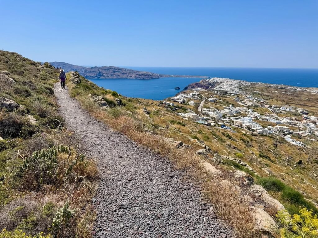 Hikers walking a gravel trail on a hillside with a blue ocean view.