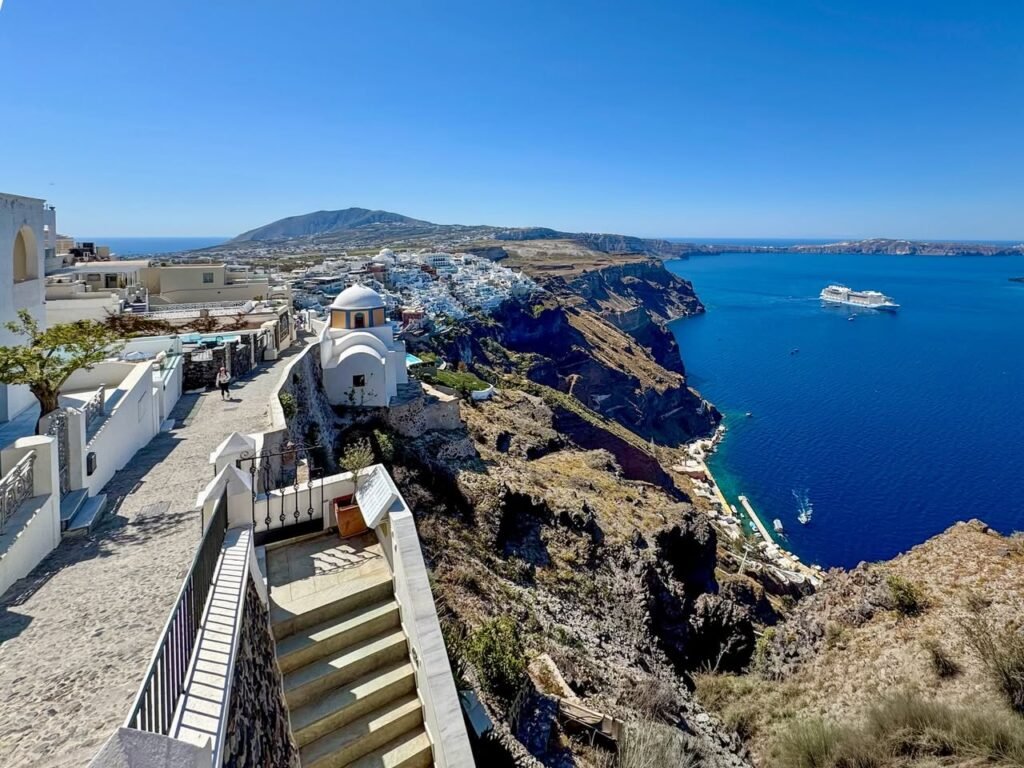 White buildings and stone pathways on cliffs overlooking the deep blue Aegean Sea.