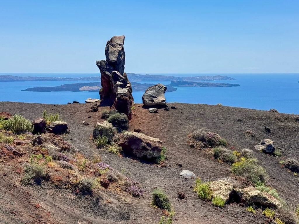 Stone sculptures standing on a rocky outcrop overlooking deep blue bodies of water under a clear sky