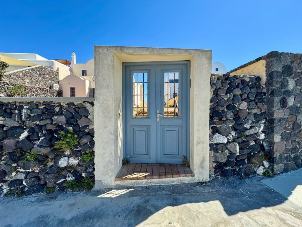 A pair of gray double doors set in a stone wall, with clear blue sky above.