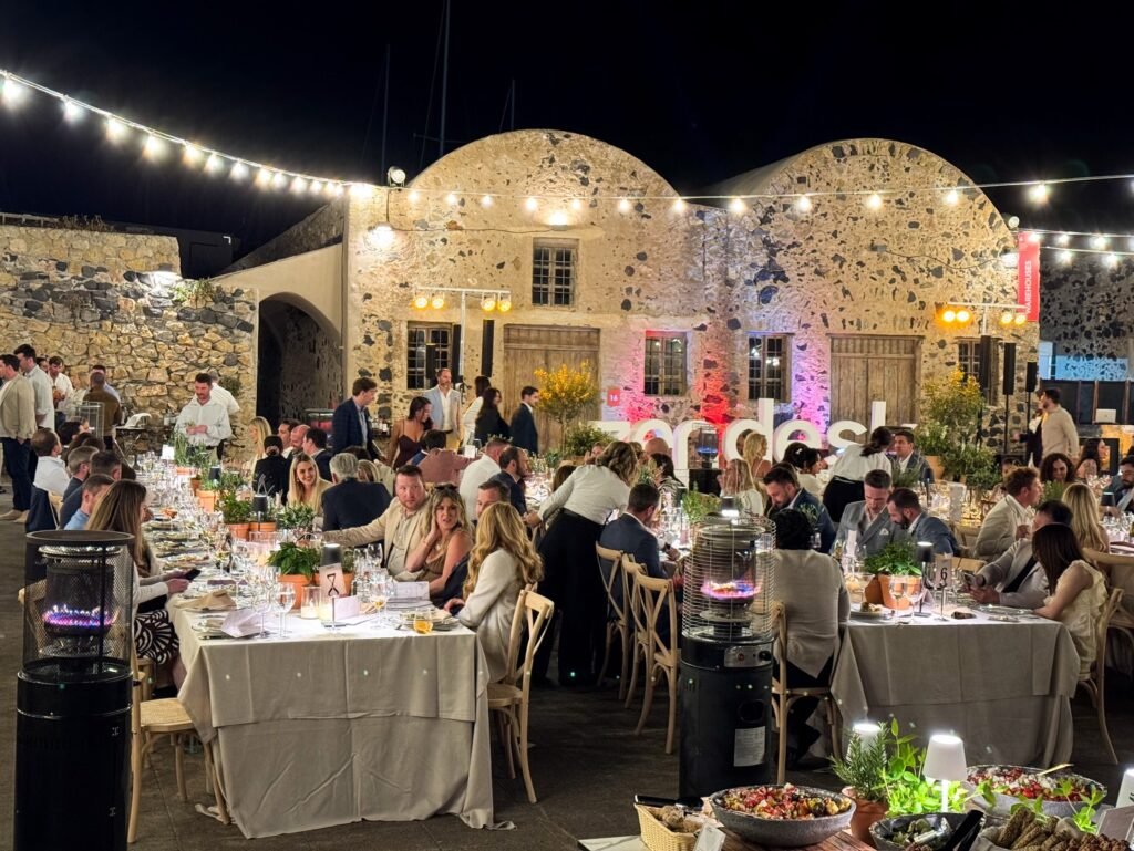 Guests seated at a formal outdoor dinner in front of unique Venetian shell architecture adorned with string lights.