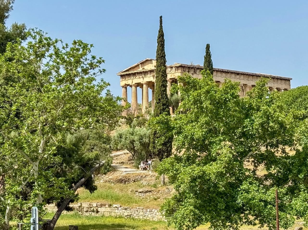 Athens Ancient Greek temple atop a hill surrounded by lush green trees and cypress, under a clear sky.