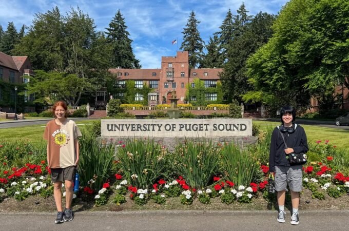 Individuals standing in front of the University of Puget Sound entrance sign, with a view of the campus architecture and background.