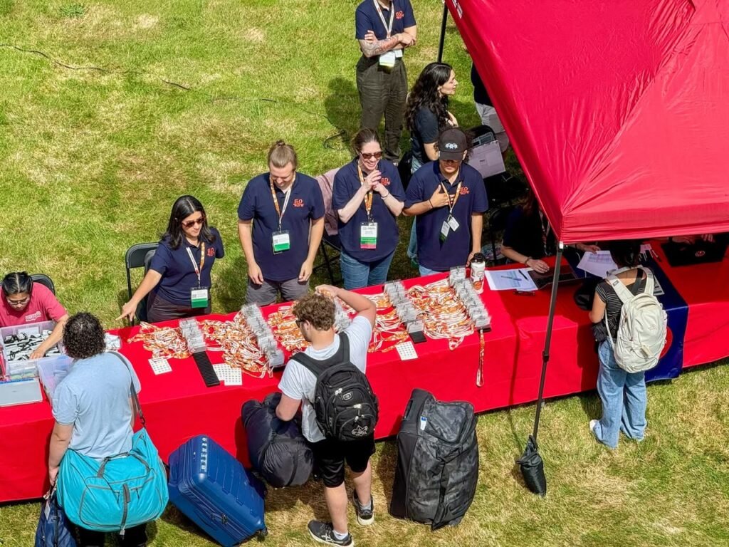 An overhead view of a red canopy tent at an outdoor market, with staff members in navy blue shirts arranging crafts on red tables that are browsing items.