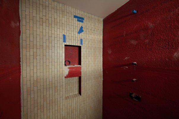 A wall of beaded glass illuminated in red with a projection of blue shapes on a white brick wall.