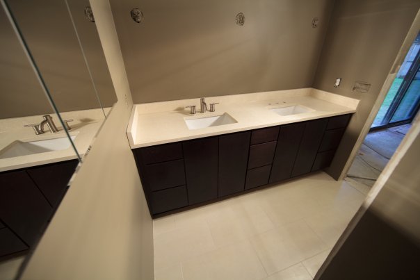A view of a modern bathroom featuring a dual-sink vanity with white countertops and dark wood cabinetry. The space includes a large mirror and a sliding glass door leading outside.
