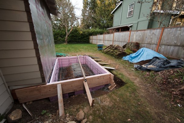 A backyard scene featuring wooden fish ponds alongside a garden and a blue tarp.