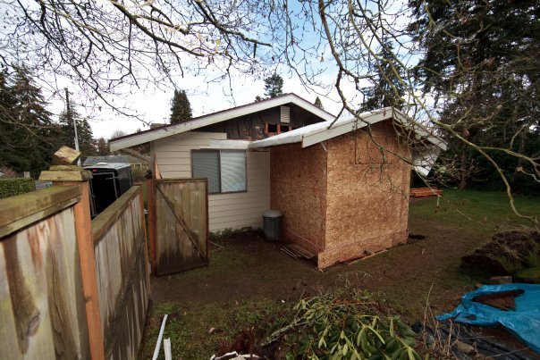 A residential backyard with a damaged structure, downed branches, and a blue tarp.