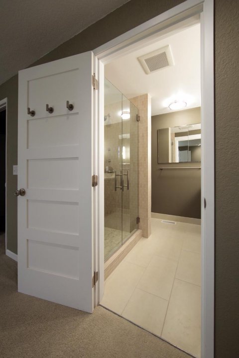 A view through an open white door into a newly remodeled bathroom with tiled floors and glass shower enclosure.