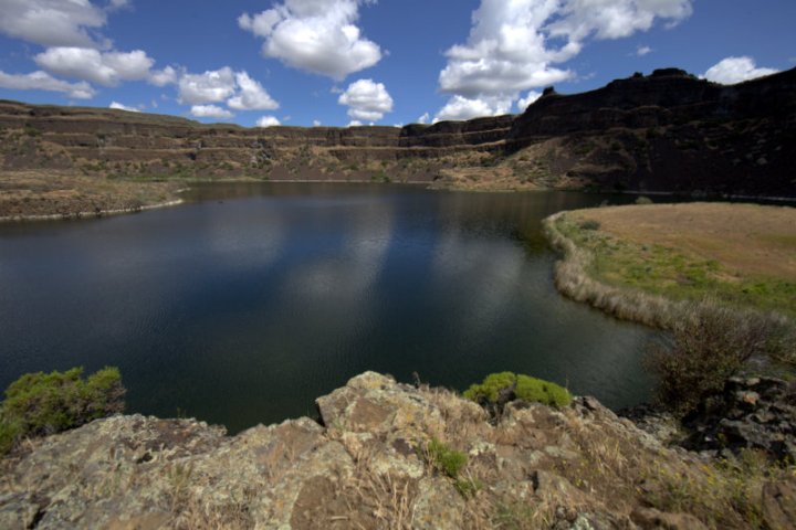 A panoramic view of a calm lake nestled in a rugged basin under a blue sky.