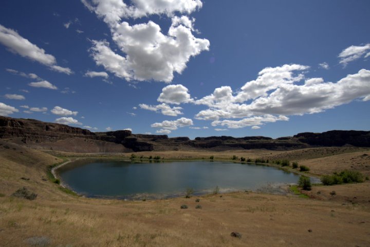 A secluded pond nestled in a dry landscape under a vibrant blue sky with white clouds.