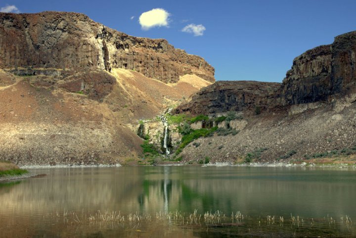 Aerial view of a waterway winding through a rocky desert landscape, framed by cliffs and a clear blue sky.