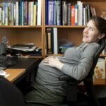 A person relaxing in a chair before a bookshelf at an office desk.