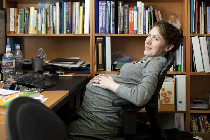 A person relaxing in a chair before a bookshelf at an office desk.
