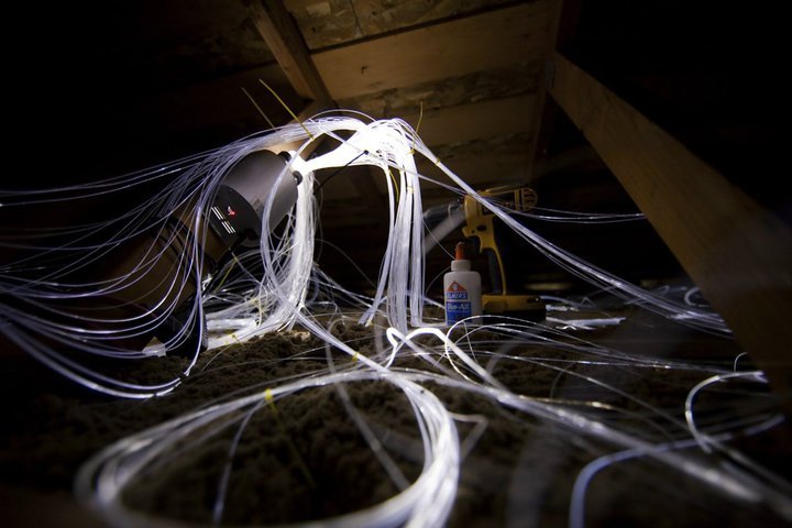 Tangled white fiber optic cables draped over equipment in a dimly lit industrial space.