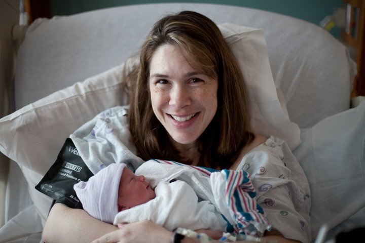 A smiling new mother cradles her newborn baby in a hospital bed.