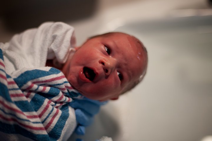 A newborn baby wrapped in a striped towel and a blue burp cloth, lying on its back.