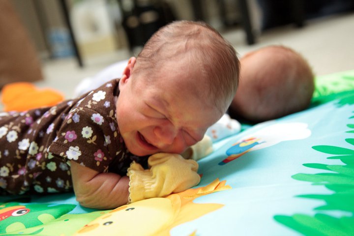 Two newborn twins resting together on a colorful play mat at home.