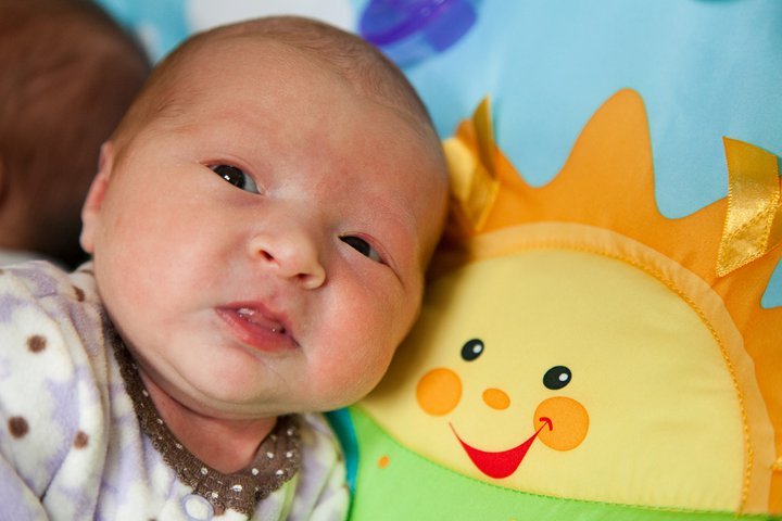 Close-up of a sleeping baby next to a colorful plush sun toy on a soft blue background.