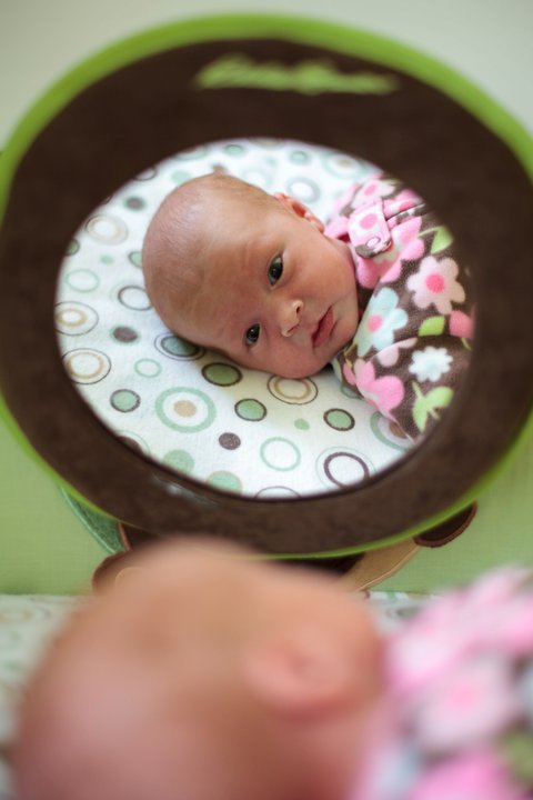 A smiling baby lies curled up on a patterned cushion in a cozy seat.