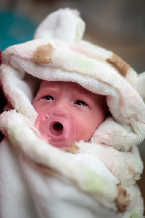 A close-up photo of a newborn baby wrapped in a soft white blanket yawning widely with eyes open.