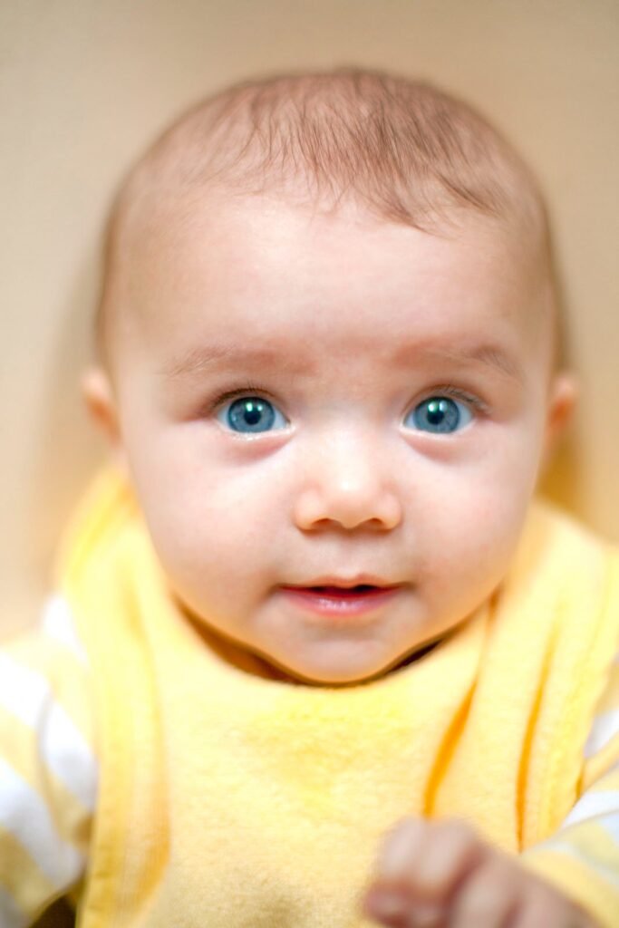 A close portrait of a baby with bright blue eyes wearing a yellow shirt. The image includes cropped views highlighting the facial details.