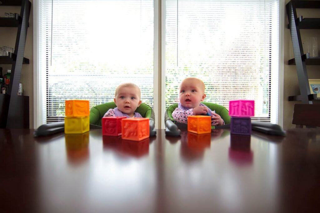 Two babies in highchairs play with colorful building blocks on a table.