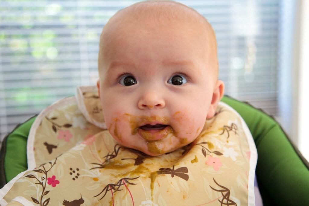 A close-up of a baby with food on their face wearing a decorative bib in a high chair.
