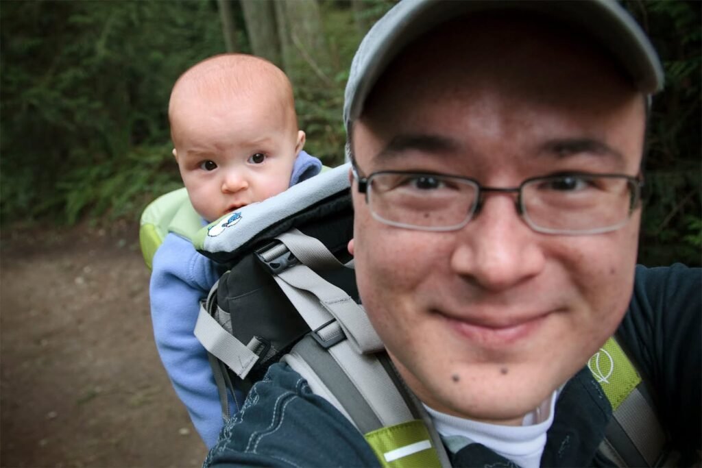 A parent carries a baby in a backpack while walking on a forest trail.