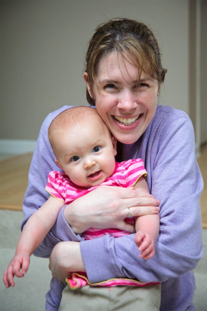 A woman joyfully holds a baby in a pink outfit. The scene is filled with warmth and happiness.