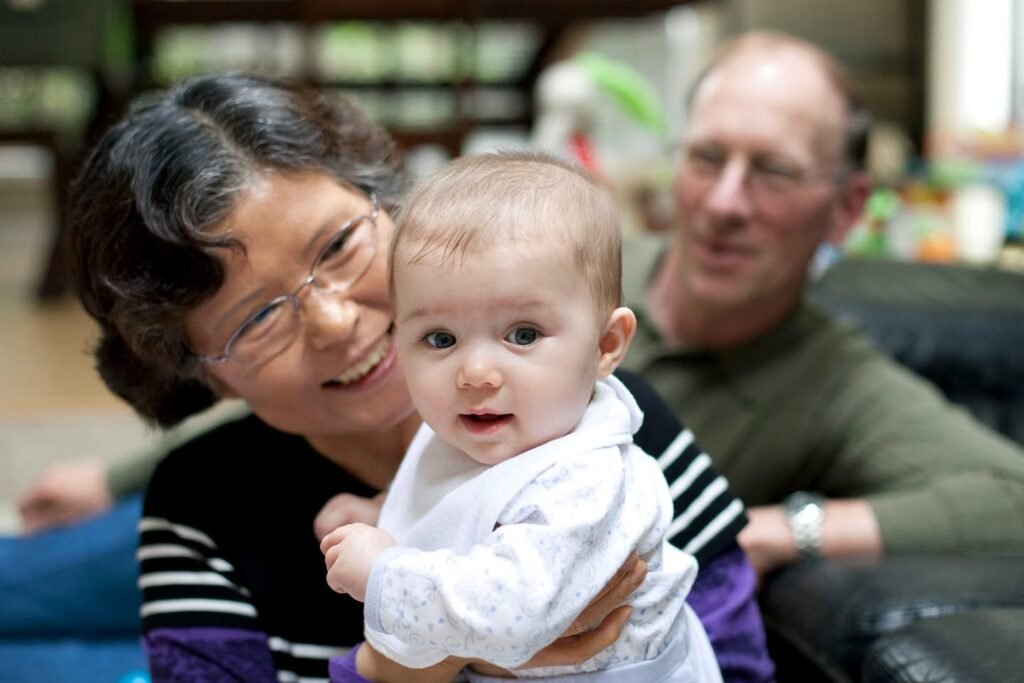 A woman holds a baby in her arms while a man looks on, capturing a tender family moment indoors.