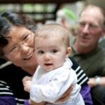 A woman holds a baby in her arms while a man looks on, capturing a tender family moment indoors.