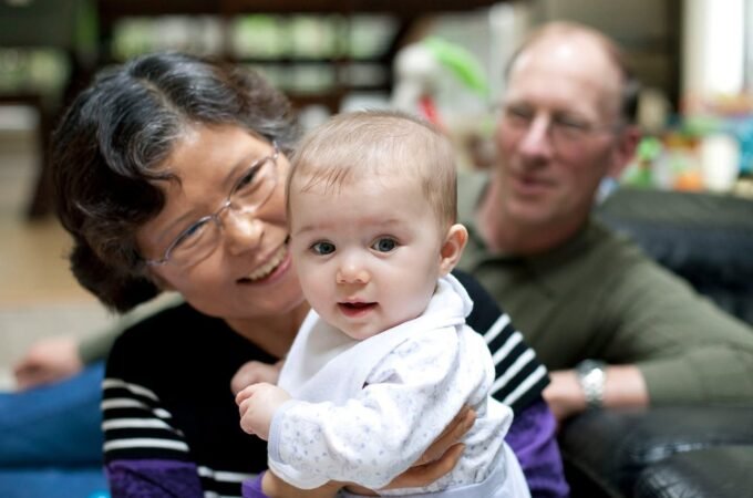A woman holds a baby in her arms while a man looks on, capturing a tender family moment indoors.