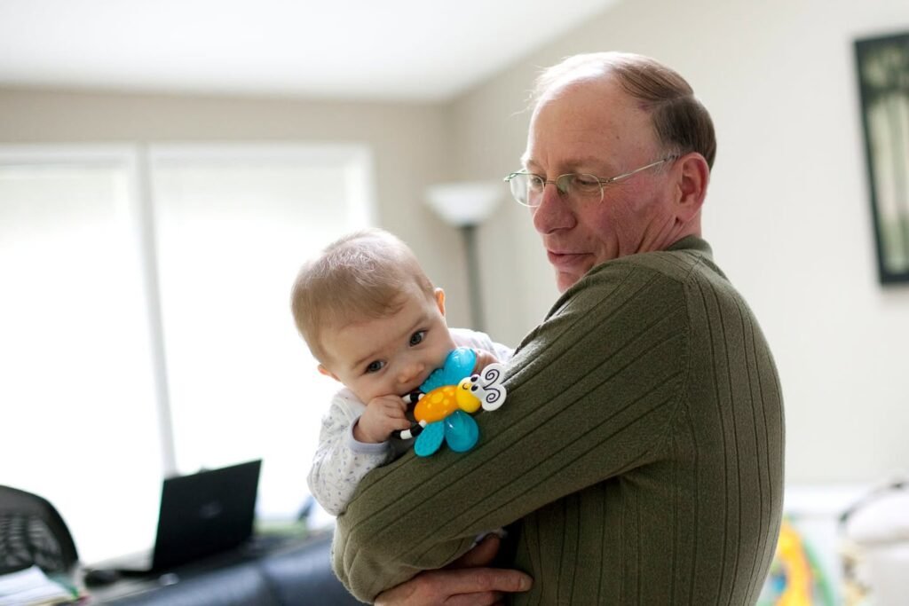 A grandfather holds a baby who is holding a colorful toy in an indoor setting.