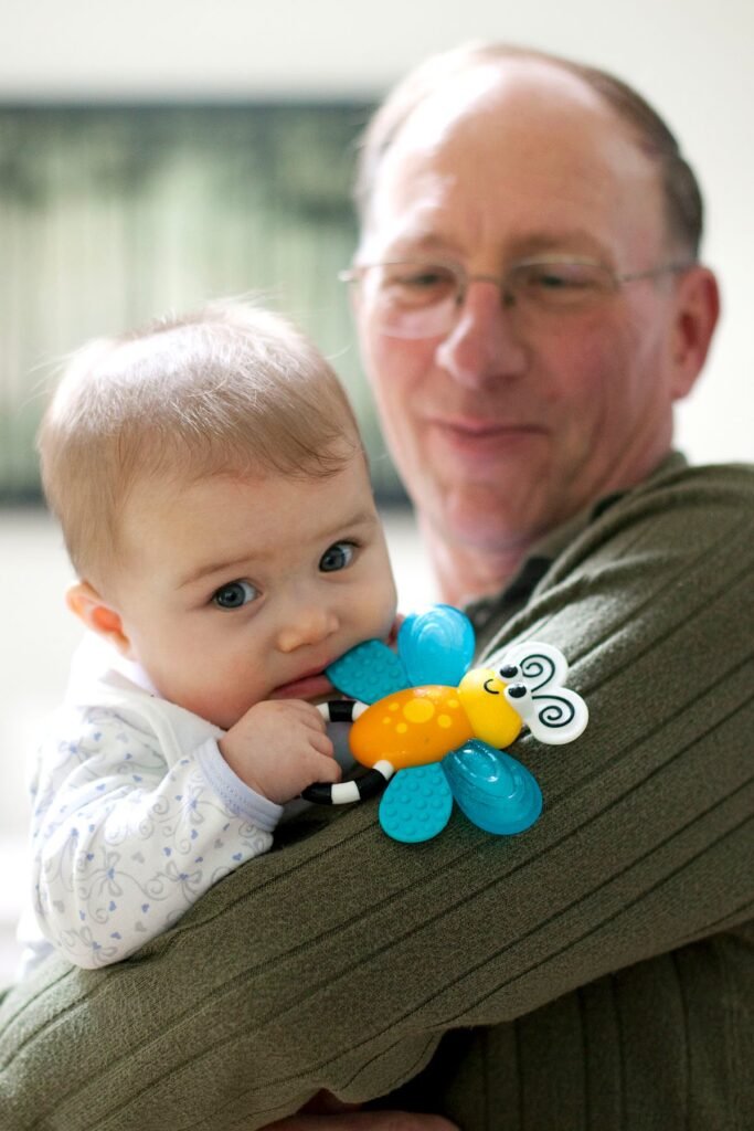 A loving portrait of a grandparent holding a baby while they chew on a colorful butterfly teether.