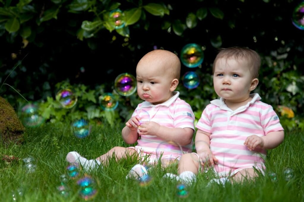 Two small children sitting on green grass surrounded by floating soap bubbles.
