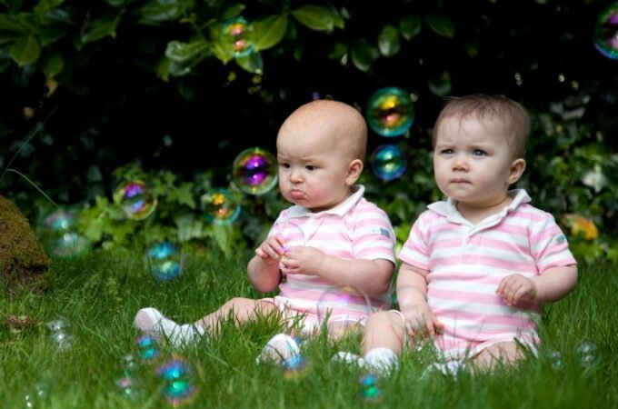 Two small children sitting on green grass surrounded by floating soap bubbles.