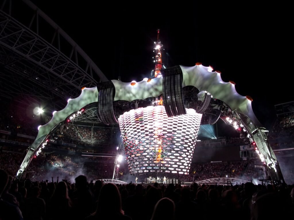 Dramatic nighttime views of a large concert stage, featuring bright lights and silhouettes of an engaged crowd.