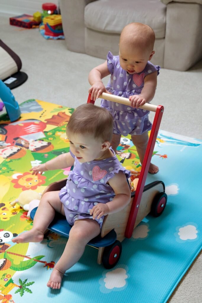 Two young children in matching outfits enjoying playtime on a colorful play mat with a push walker.