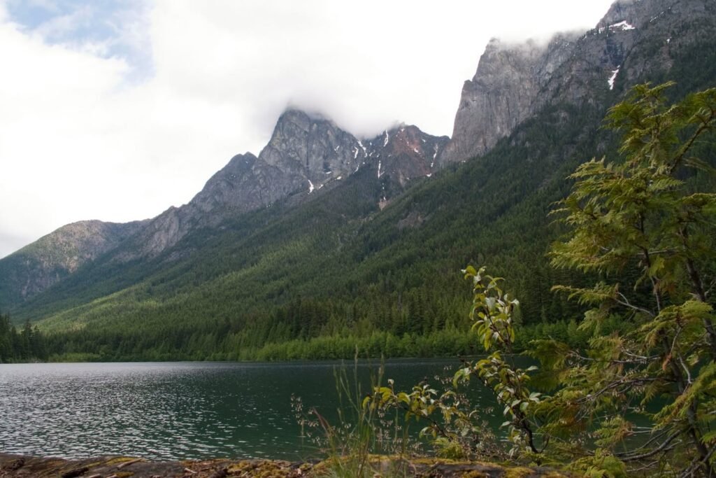 A serene mountain lake with misty peaks and lush green vegetation in the Pacific Northwest.
