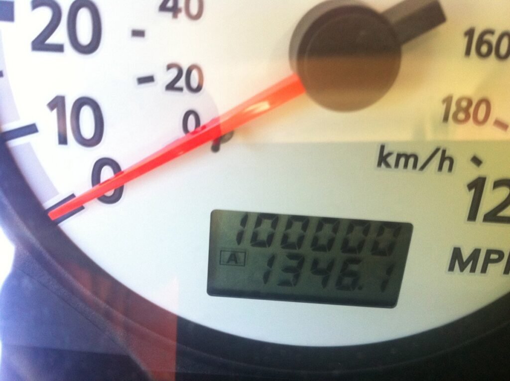 A car dashboard showing a digital odometer reaching one hundred thousand miles at rest.