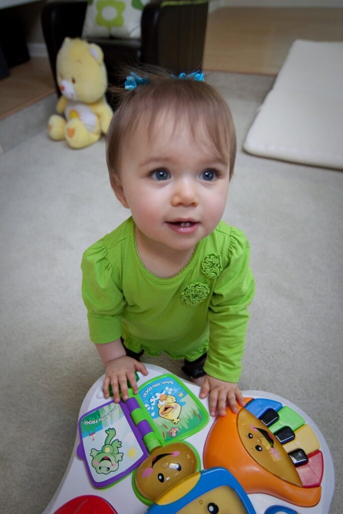A young child in a green top plays with a colorful activity mat featuring playful character designs.